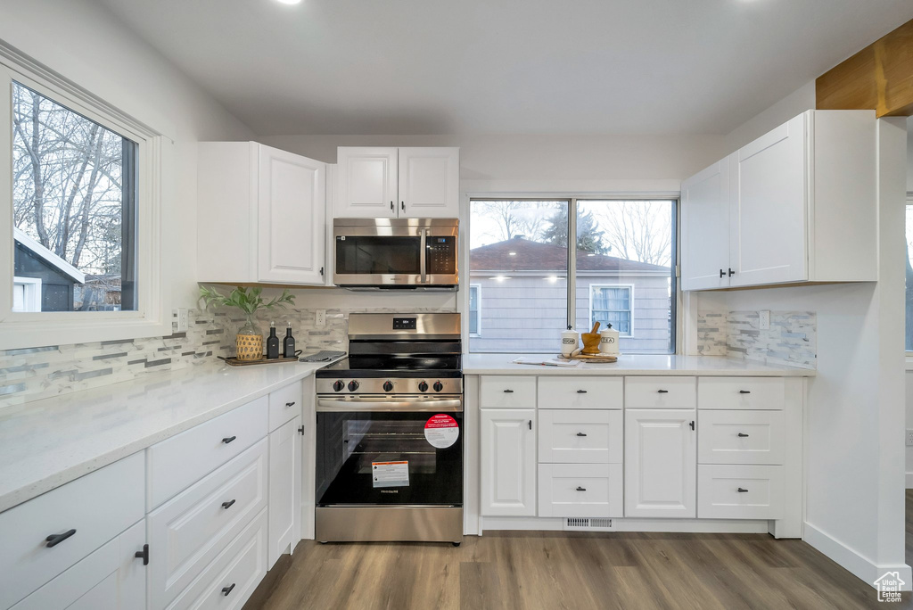 Kitchen featuring stainless steel appliances, wood finished floors, backsplash, and white cabinetry