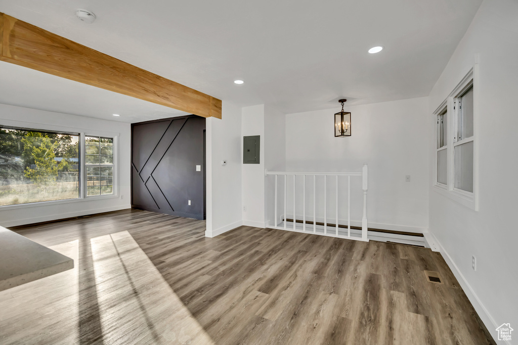 Unfurnished living room with electric panel, wood finished floors, recessed lighting, beamed ceiling, and a chandelier