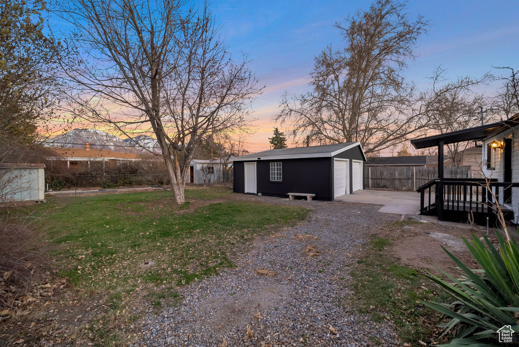 Yard at dusk with an outdoor structure, a garage, and a deck