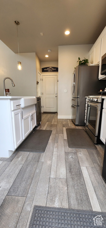 Kitchen featuring stainless steel appliances, white cabinetry, wood-type flooring, decorative light fixtures, and recessed lighting
