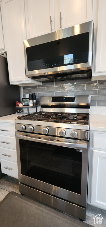 Kitchen with stainless steel appliances, white cabinets, light countertops, and decorative backsplash