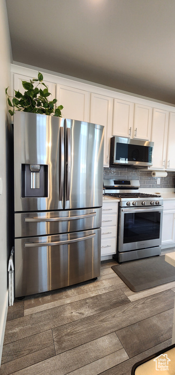 Kitchen featuring stainless steel appliances, white cabinets, decorative backsplash, and dark wood finished floors