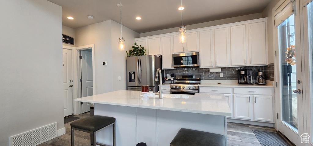 Kitchen featuring appliances with stainless steel finishes, backsplash, wood finished floors, white cabinetry, and a kitchen bar