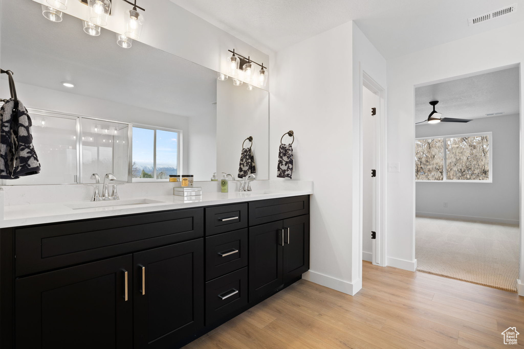 Full bath with double vanity, ceiling fan, a shower stall, and wood finished floors