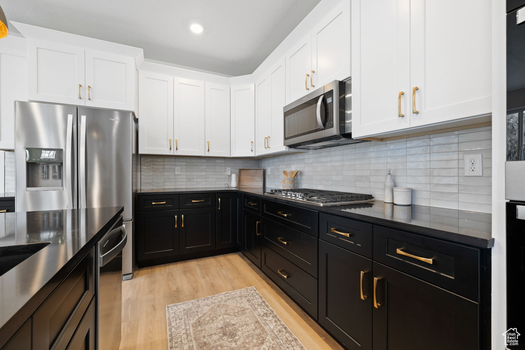 Kitchen featuring stainless steel appliances, dark cabinetry, white cabinetry, light wood finished floors, and decorative backsplash