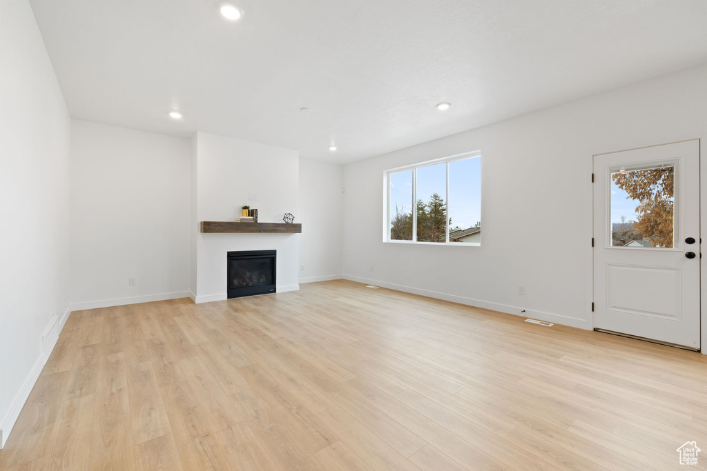 Unfurnished living room with light wood-type flooring, a glass covered fireplace, and recessed lighting