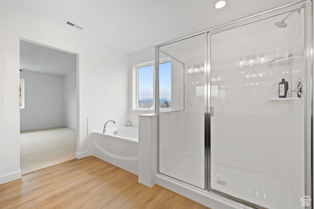 Full bath featuring a stall shower, a garden tub, and wood finished floors
