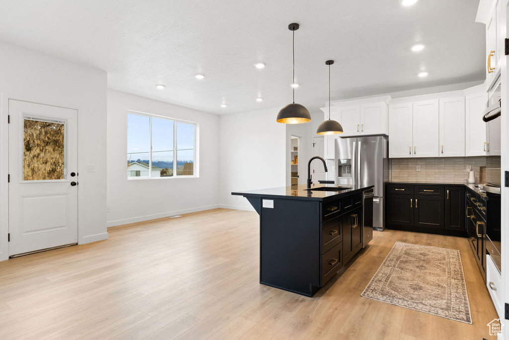 Kitchen with dark cabinets, dark countertops, light wood-style flooring, backsplash, and recessed lighting