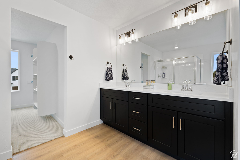 Full bath with double vanity, a stall shower, and wood finished floors