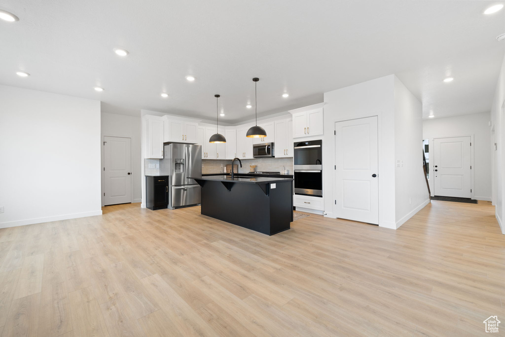 Kitchen featuring appliances with stainless steel finishes, dark countertops, a breakfast bar area, light wood-style flooring, and recessed lighting