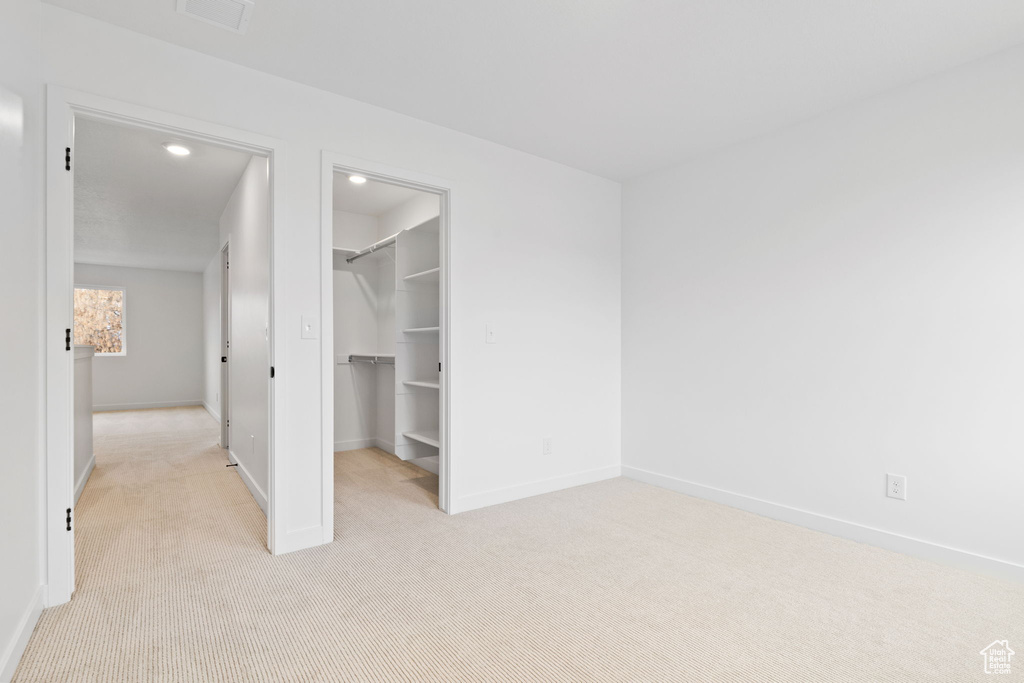 Unfurnished bedroom with light carpet, a spacious closet, recessed lighting, and a closet