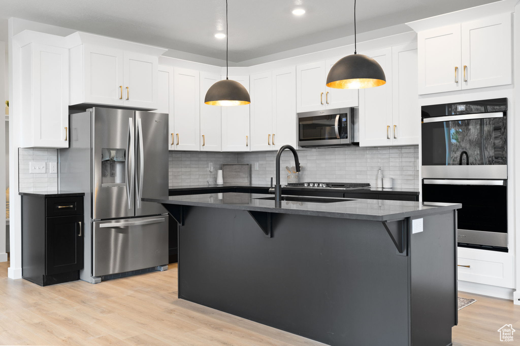 Kitchen with stainless steel appliances, decorative backsplash, a breakfast bar, light wood-style floors, and recessed lighting