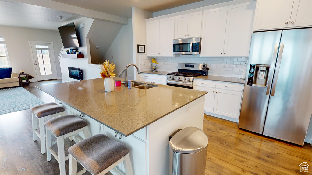 Kitchen featuring appliances with stainless steel finishes, light wood-style floors, decorative backsplash, and white cabinetry