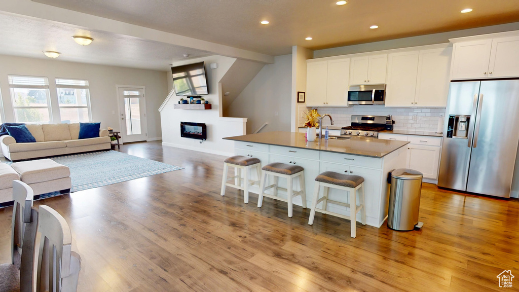 Kitchen featuring stainless steel appliances, open floor plan, a kitchen breakfast bar, tasteful backsplash, and light wood finished floors