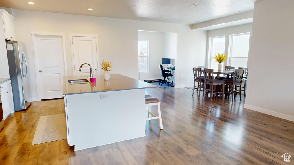 Kitchen with freestanding refrigerator, white cabinets, a center island with sink, light wood-type flooring, and a kitchen bar