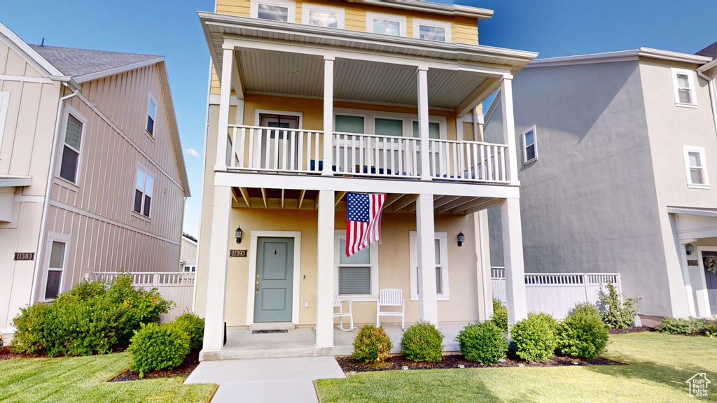 View of front of property featuring a balcony, a porch, and a front lawn