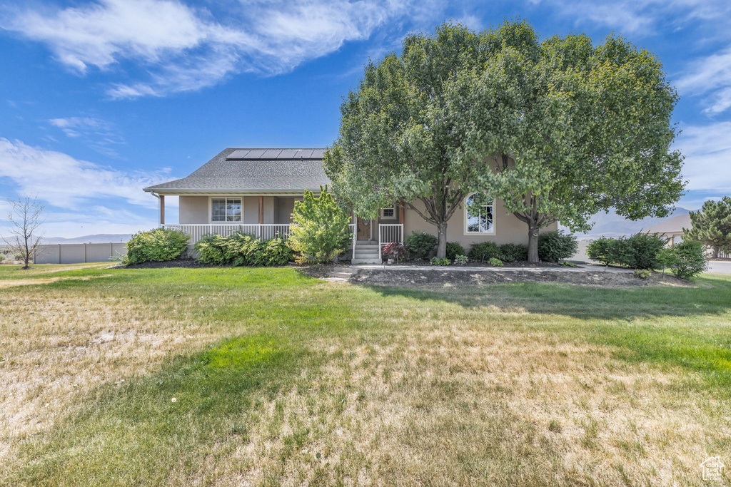 View of front of house featuring roof mounted solar panels, covered porch, a front lawn, and stucco siding