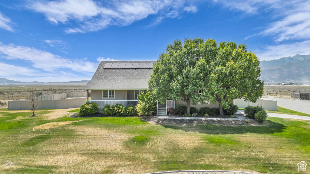 View of front of house with a mountain view, roof mounted solar panels, a porch, and a shingled roof