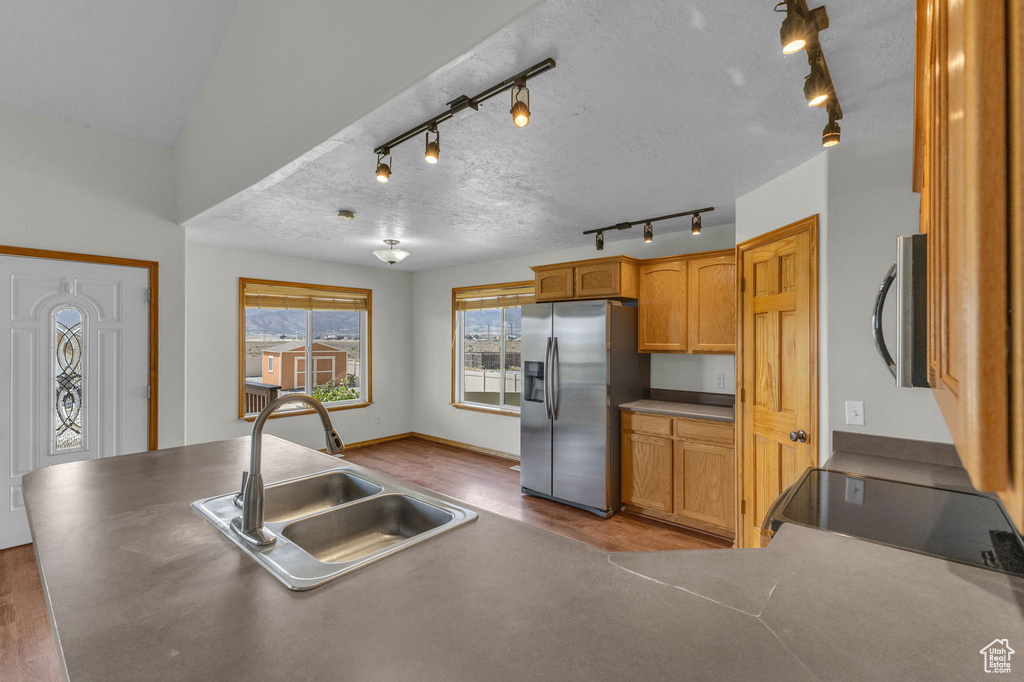 Kitchen featuring stainless steel appliances, track lighting, wood finished floors, and brown cabinetry