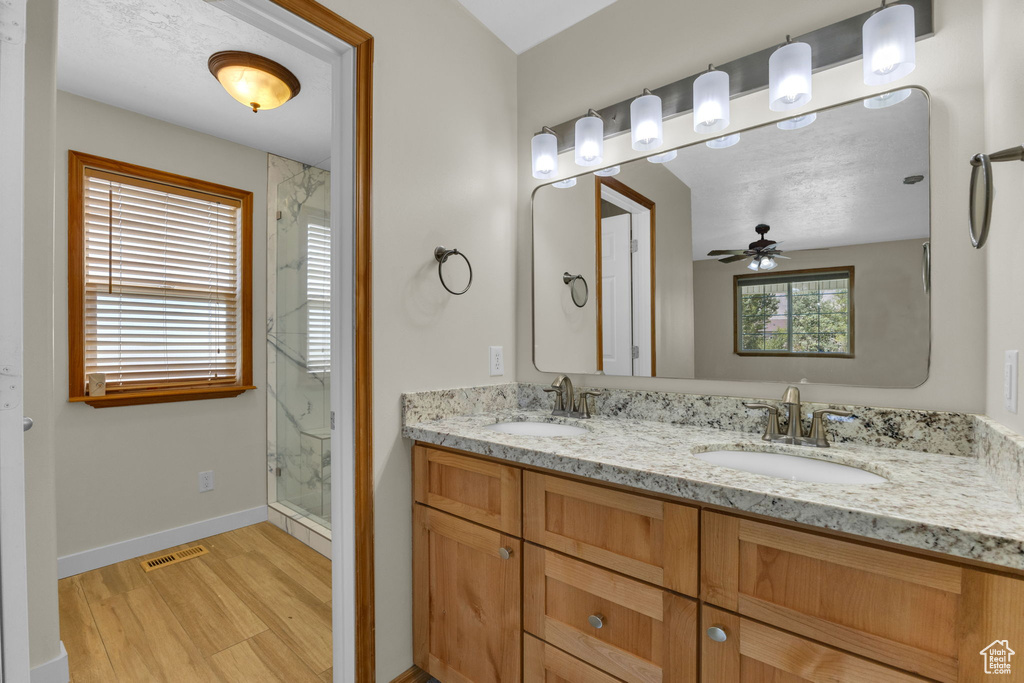 Full bath with a marble finish shower, wood finished floors, double vanity, and ceiling fan
