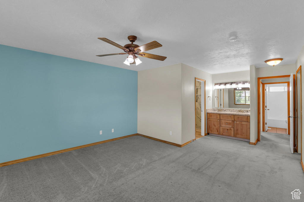Unfurnished bedroom with light colored carpet, ensuite bathroom, and a textured ceiling