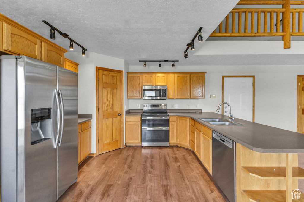 Kitchen featuring appliances with stainless steel finishes, track lighting, a peninsula, open shelves, and a textured ceiling