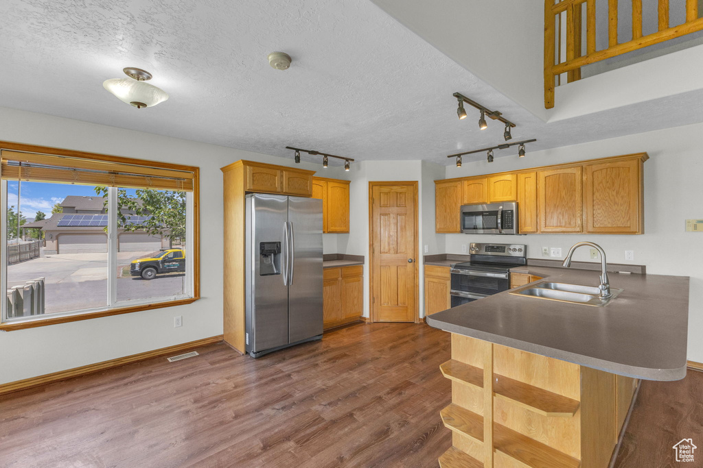 Kitchen featuring appliances with stainless steel finishes, rail lighting, dark wood-type flooring, dark countertops, and a peninsula