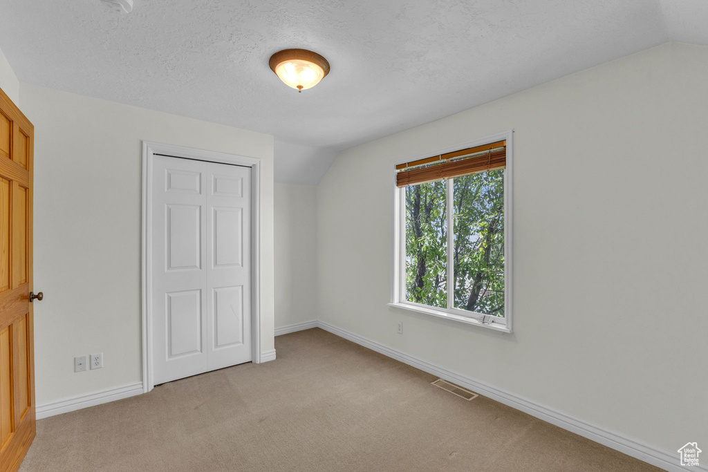 Unfurnished bedroom featuring light carpet, a closet, and lofted ceiling