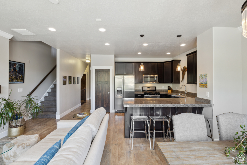 Kitchen with appliances with stainless steel finishes, light wood-type flooring, a breakfast bar, a peninsula, and dark brown cabinetry