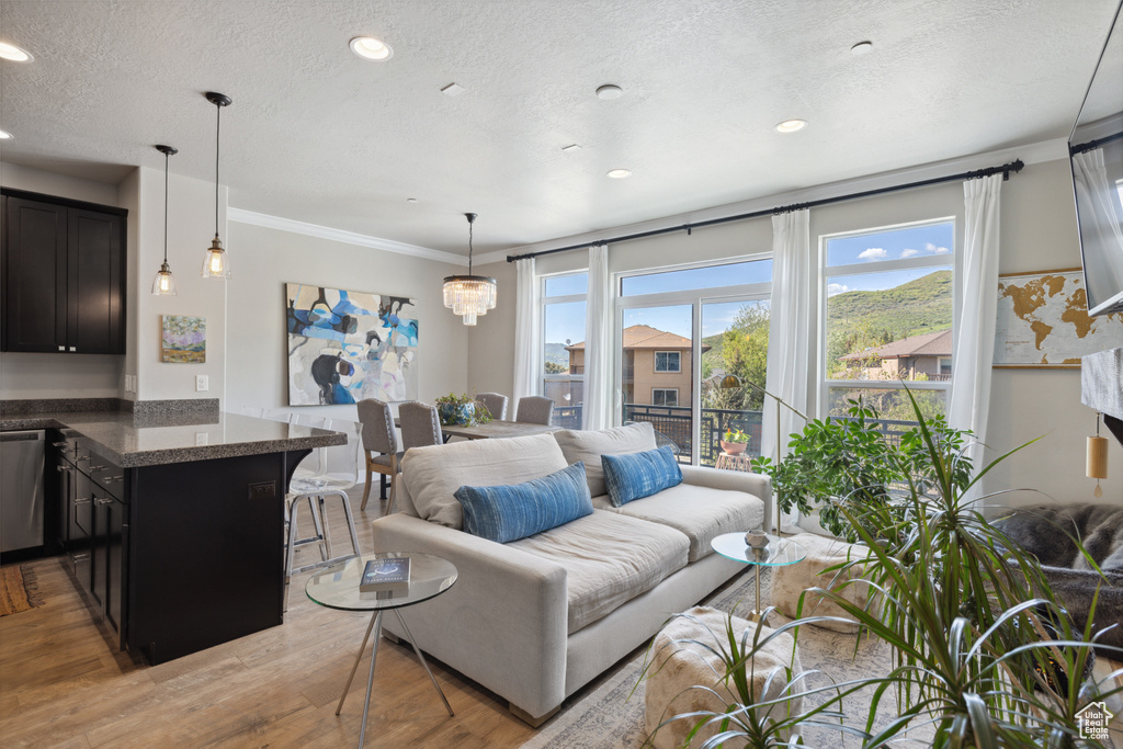 Living room with light wood finished floors, crown molding, a textured ceiling, and recessed lighting