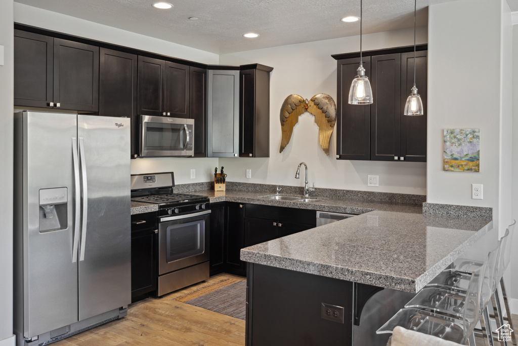 Kitchen featuring appliances with stainless steel finishes, a peninsula, a kitchen breakfast bar, light wood-style floors, and pendant lighting