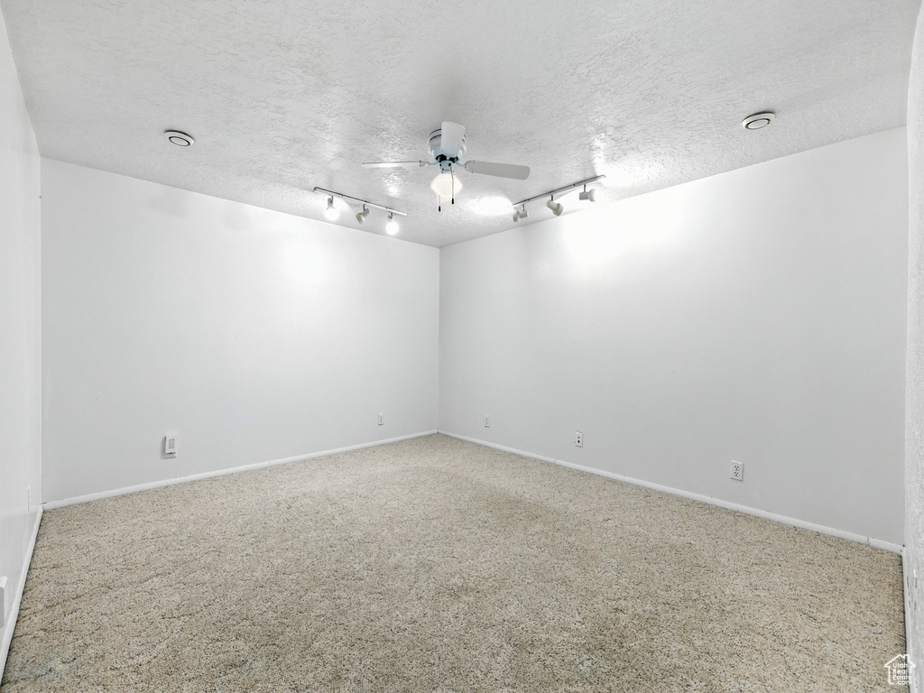 Empty room featuring a ceiling fan, carpet flooring, a textured ceiling, and rail lighting