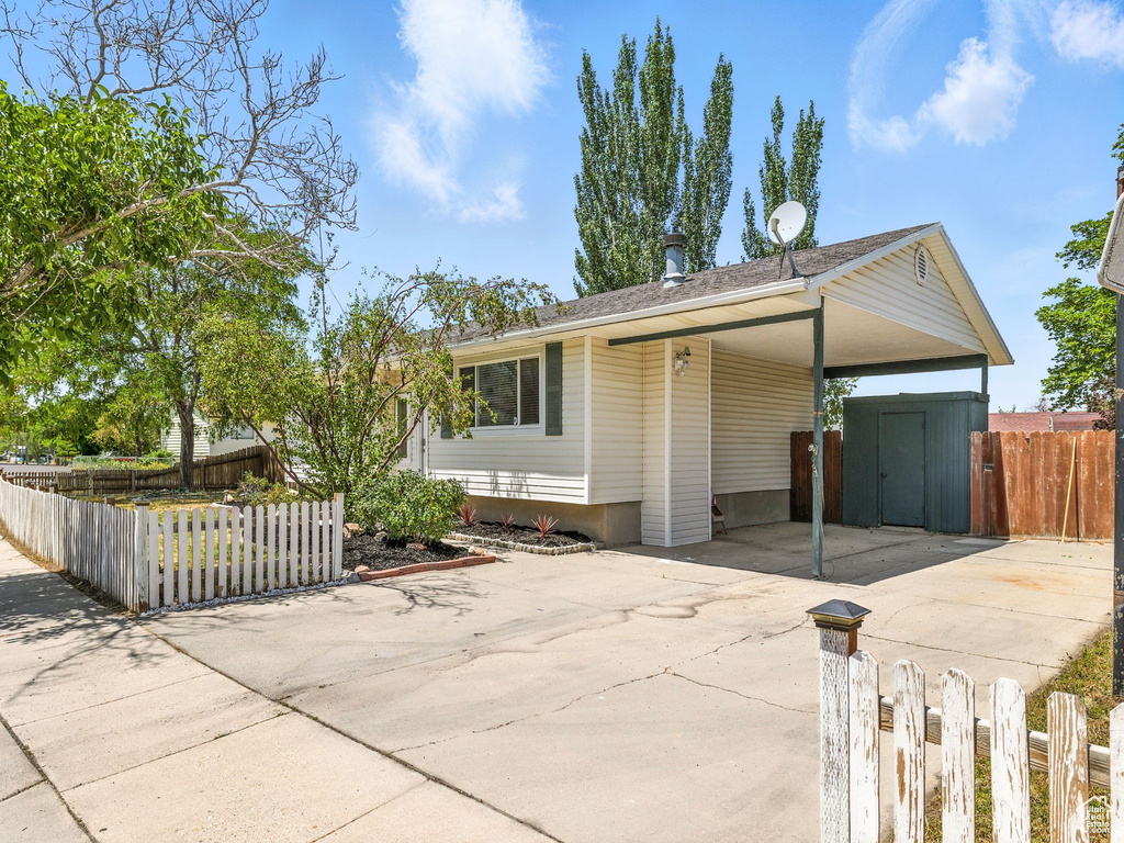 Ranch-style home featuring driveway, a fenced front yard, a carport, and a shed