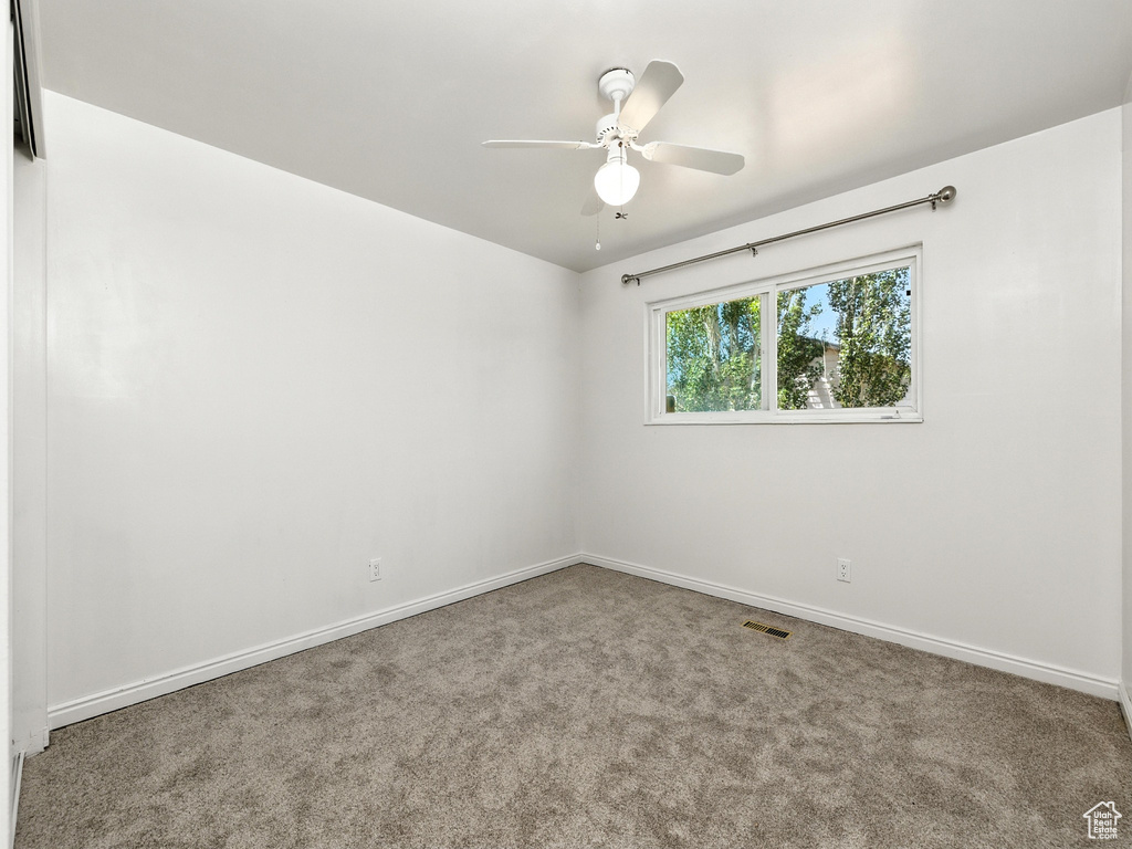 Carpeted spare room featuring ceiling fan and baseboards