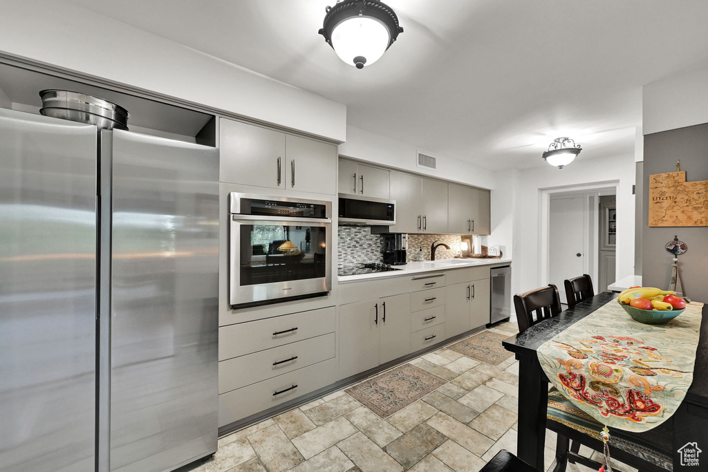 Kitchen featuring stainless steel appliances, tasteful backsplash, gray cabinets, light countertops, and stone tile flooring