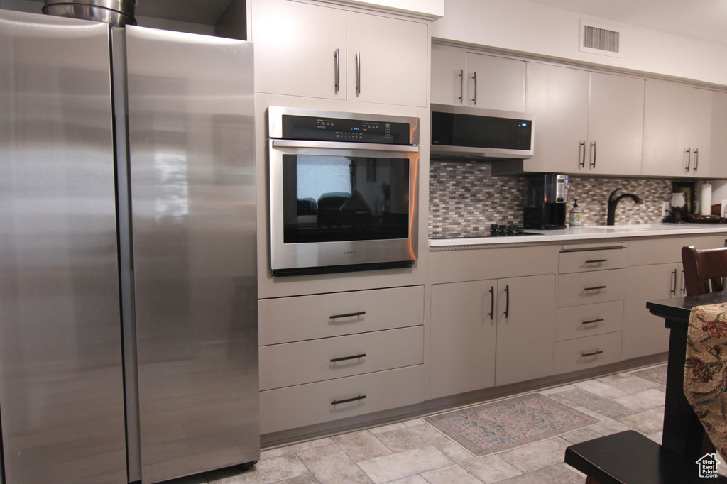 Kitchen with stainless steel appliances, tasteful backsplash, stone finish flooring, and light countertops