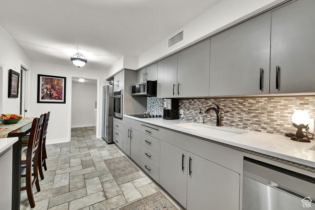 Kitchen featuring appliances with stainless steel finishes, tasteful backsplash, light countertops, and gray cabinetry