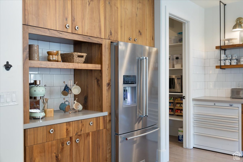 Kitchen with stainless steel appliances, open shelves, tasteful backsplash, brown cabinets, and light countertops
