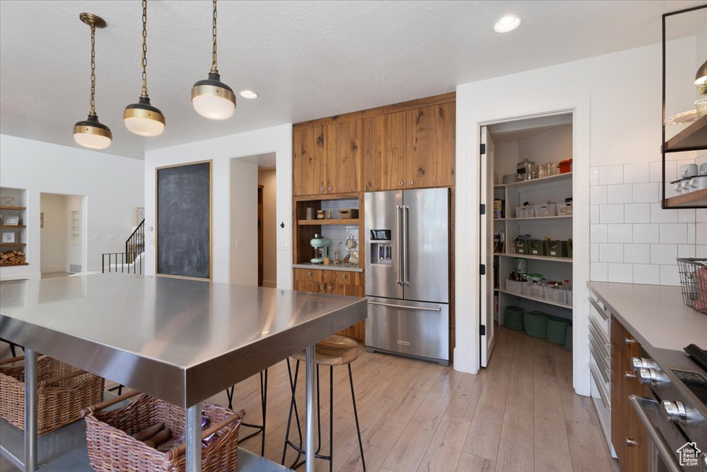 Kitchen with high end fridge, brown cabinets, open shelves, light wood-style flooring, and recessed lighting