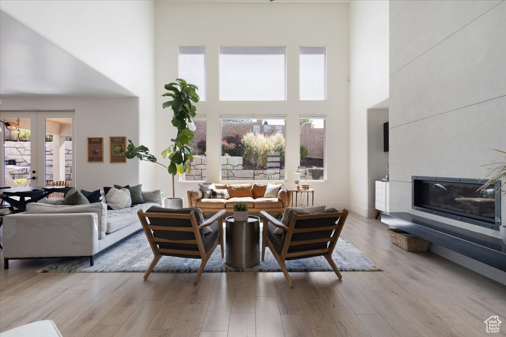Living room with a towering ceiling, wood finished floors, a glass covered fireplace, and french doors