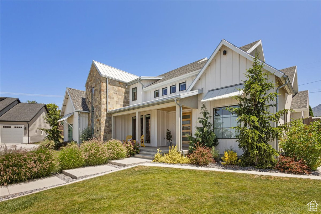 View of front of property with board and batten siding, a standing seam roof, a front yard, a porch, and a metal roof