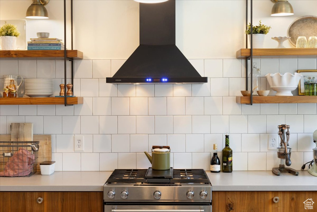 Kitchen featuring wall chimney range hood, gas range, open shelves, and brown cabinets