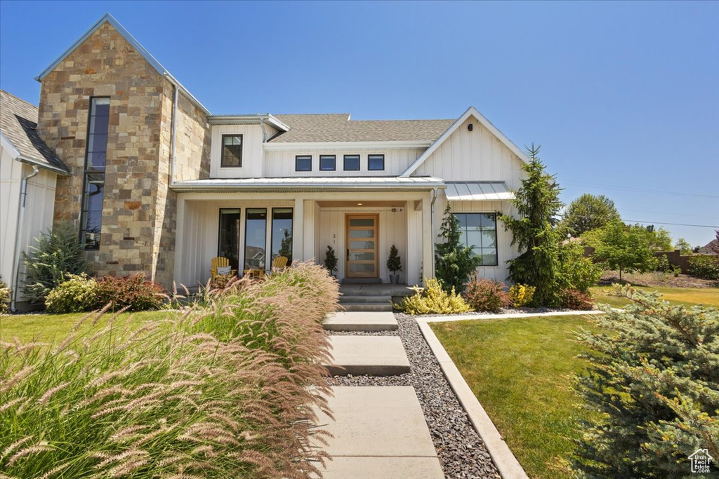 View of front of home featuring board and batten siding, a standing seam roof, a front yard, a shingled roof, and a metal roof