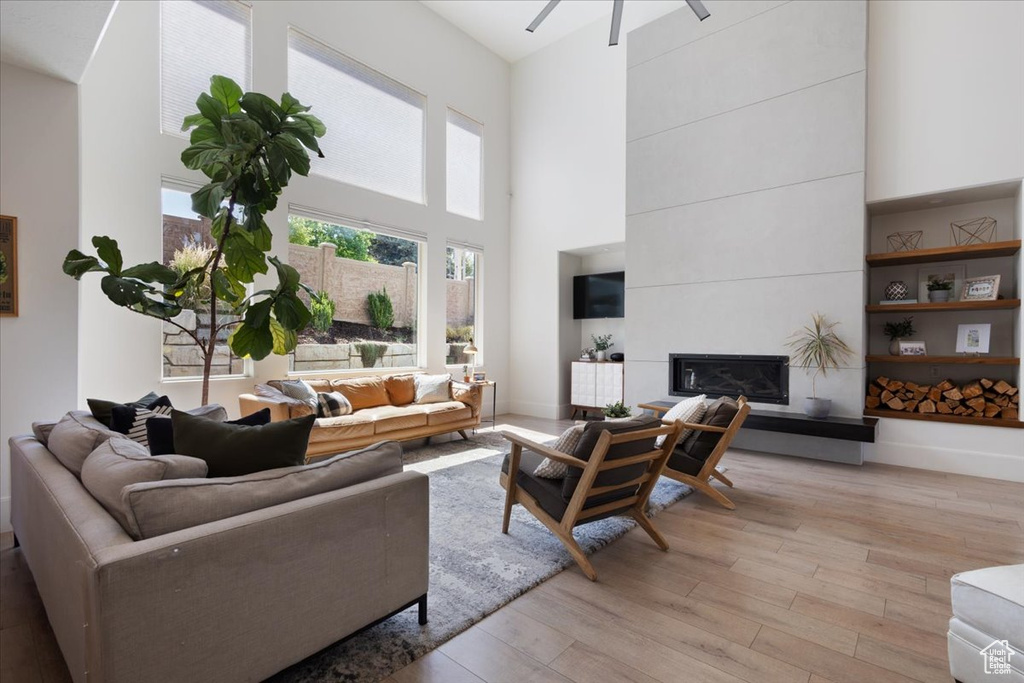 Living room with light wood finished floors, a high ceiling, a tiled fireplace, and ceiling fan