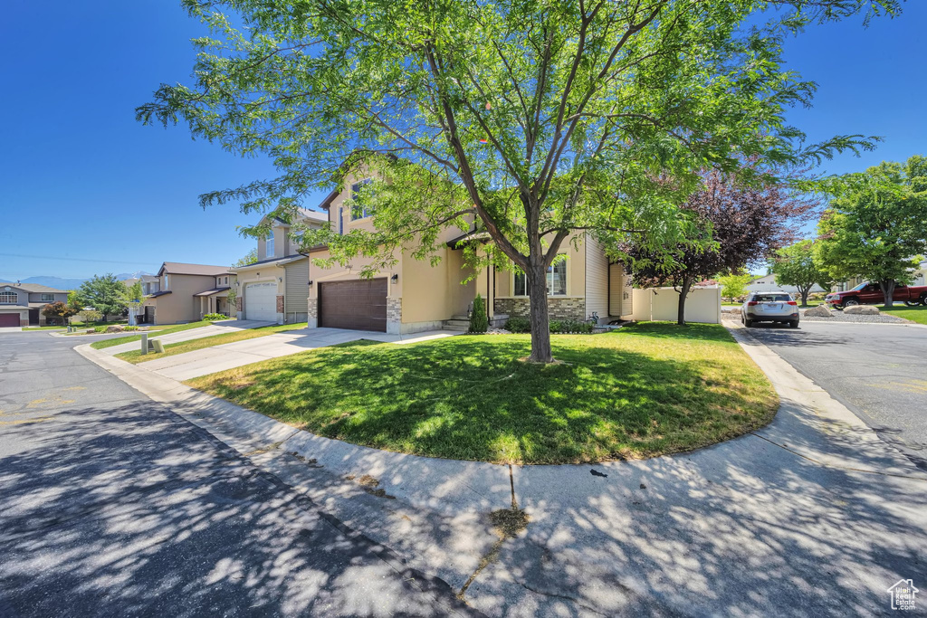 View of property hidden behind natural elements featuring driveway, a front yard, stone siding, stucco siding, and a residential view