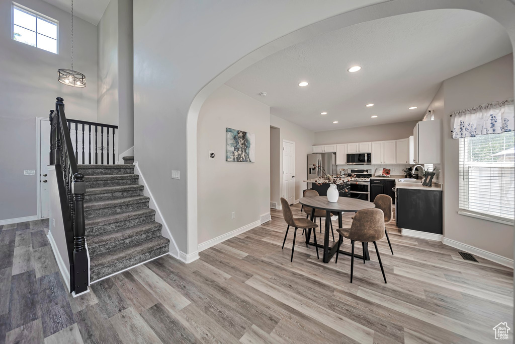 Dining space with arched walkways, light wood-style floors, healthy amount of natural light, recessed lighting, and stairway