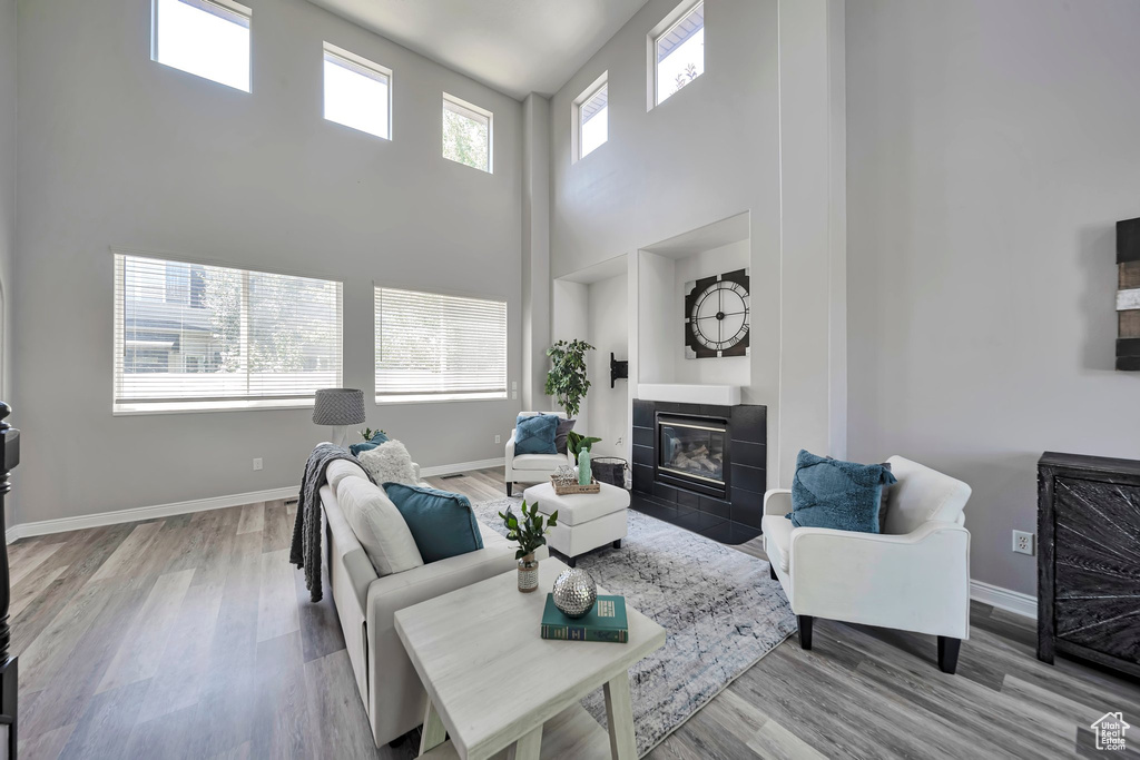 Living area with a towering ceiling, a tile fireplace, and wood finished floors