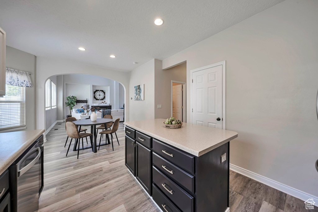 Kitchen featuring arched walkways, dishwasher, dark cabinets, light countertops, and light wood-style flooring