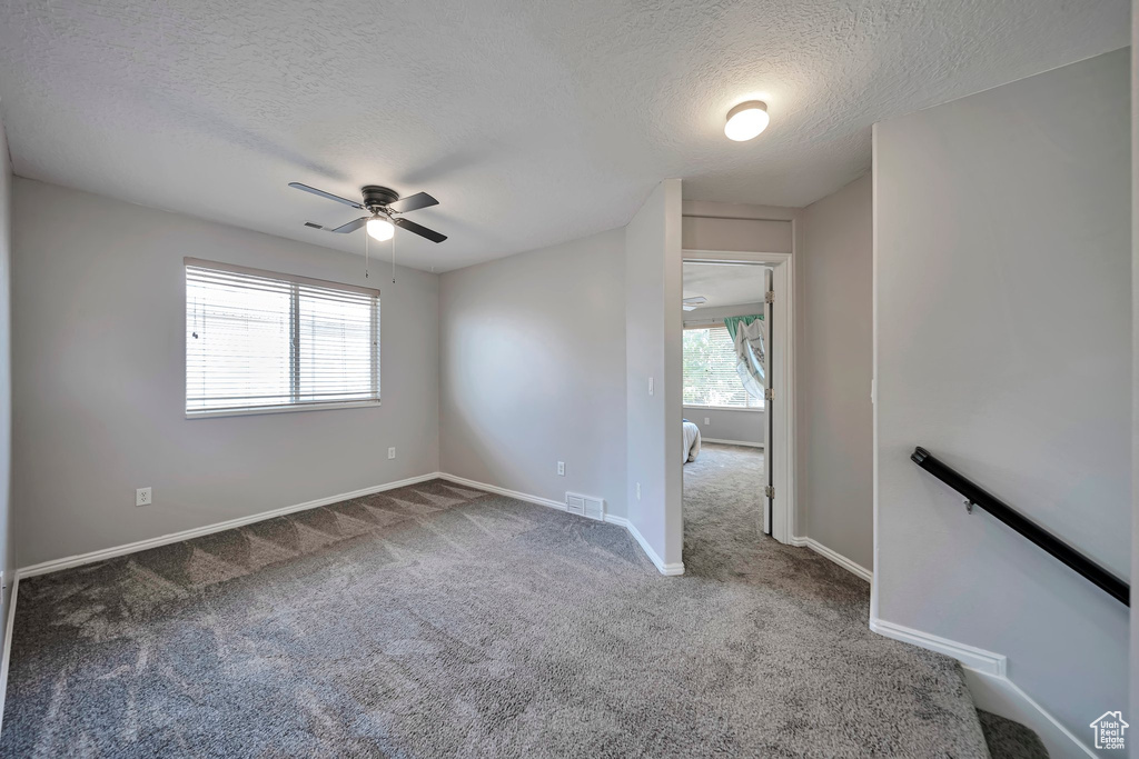 Carpeted empty room featuring a textured ceiling and ceiling fan