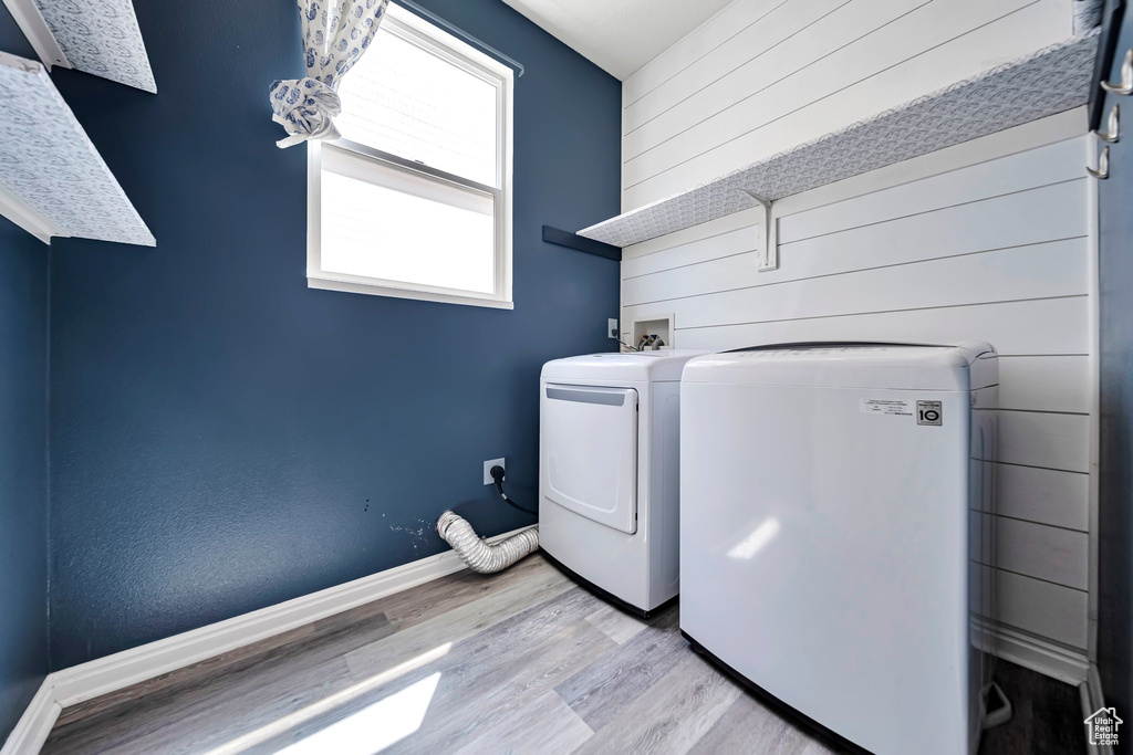 Laundry room with washing machine and dryer, light wood-type flooring, and wood walls
